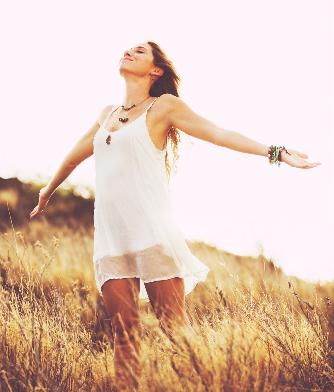 Joyful woman in a white dress standing in a golden field, arms stretched wide as she embraces the sunlight and nature around her. This serene and freeing moment reflects the rejuvenation and energy Miraculous Health provides through their finest vitamins and supplements. Fuel your health and wellness journey today by visiting MiraculousHealth.org!